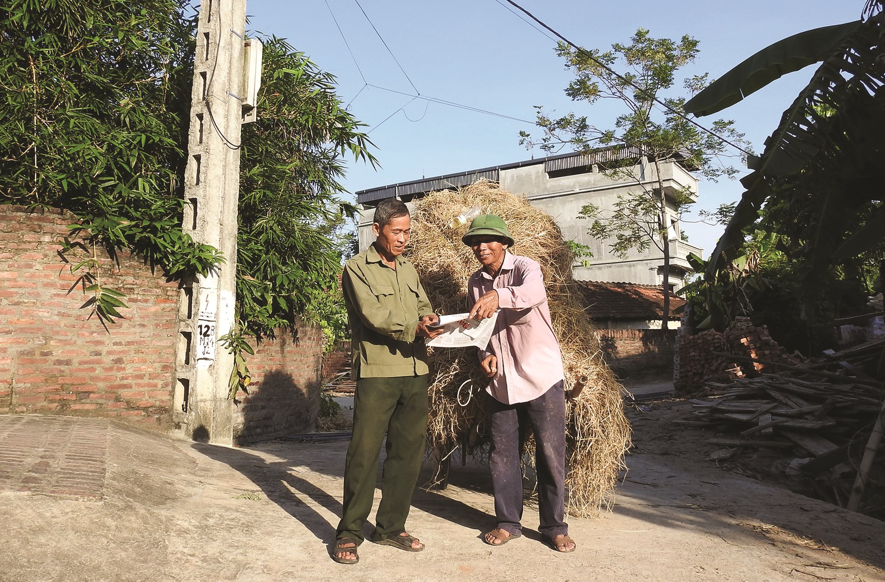 Ông Bằng Văn Ngọc (bên trái) chia sẻ thông tin trên Báo Dân tộc và Phát triển với người dân trong thôn