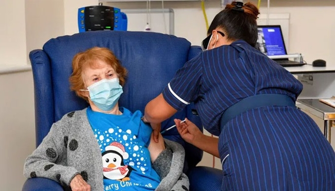 Cụ bà Margaret Keenan (90 tuổi) trở thành người đầu tiên trên thế giới được tiêm chủng COVID-19 bằng vaccine của hãng Pfizer, sau khi Anh chính thức khởi động chiến dịch tiêm chủng COVID-19 cho toàn dân - Ảnh: Reuters.