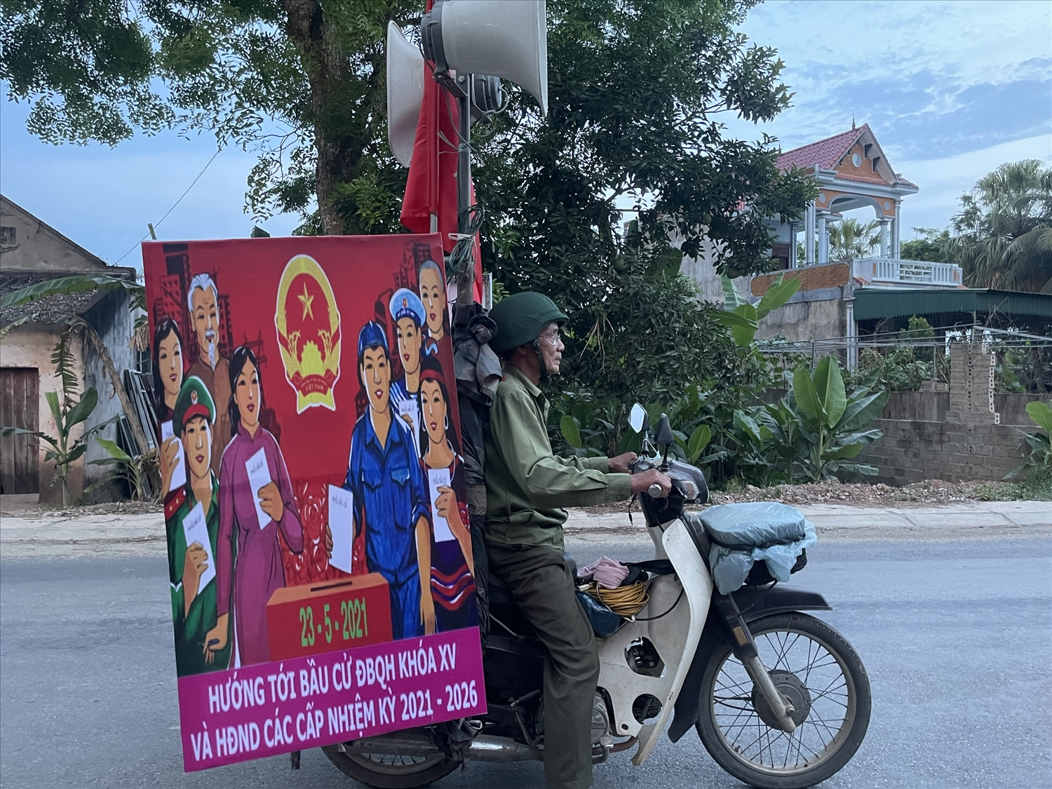Ông Phạm Ngọc Chiêng, cùng bộ loa, máy phát, cờ và băng rôn với các khẩu hiệu tuyên truyền về phòng chống dịch Covid-19, về cuộc bầu cử ĐBQH và HĐND các cấp.