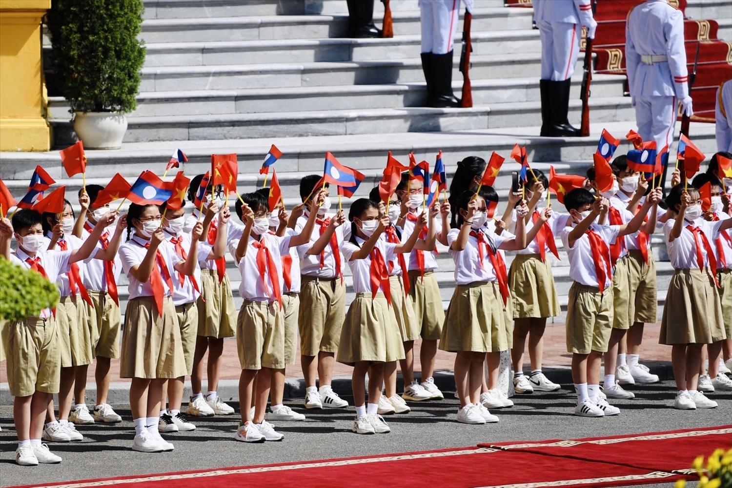 Các em thiếu niên, học sinh với cờ Việt Nam, Lào và những bông hoa tươi thắm trên tay chào đón Tổng Bí thư, Chủ tịch nước Lào cùng Phu nhân và Đoàn đại biểu Cấp cao Đảng, Nhà nước Lào - Ảnh: VGP/Nhật Bắc 