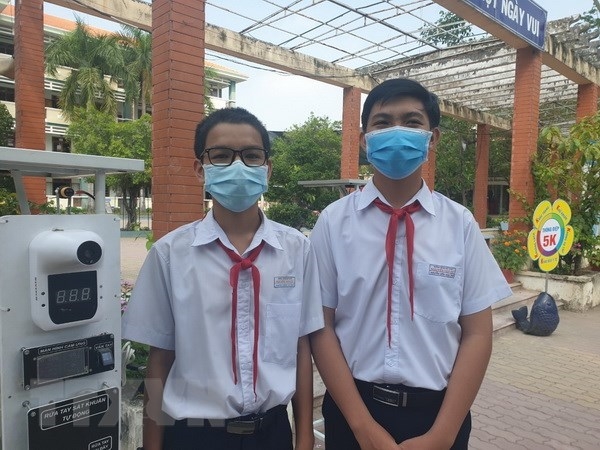 Em Nguyễn Thành Tài và em Nguyễn Điền Nam, Trường THCS Nguyễn Văn Cừ bên cạnh thiết bị đọc thân nhiệt và khử khuẩn tự động kết hợp điểm danh thông minh. Ảnh: TTXVN