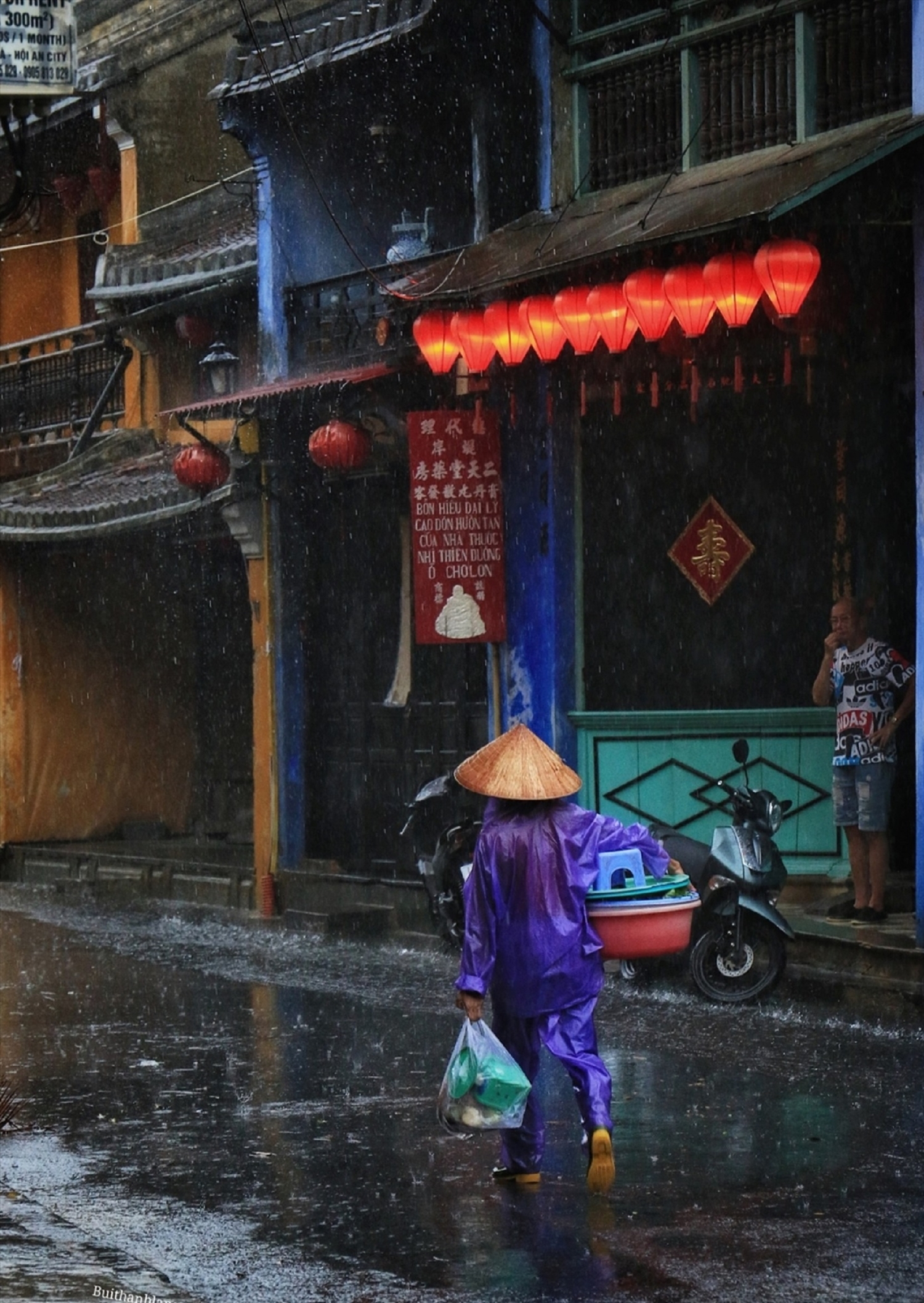 Một người phụ nữ đi bán hàng trong mưa dưới mái hiên cổ