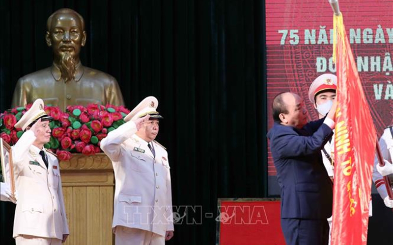Chủ tịch nước Nguyễn Xuân Phúc gắn Huân chương Chiến công hạng Nhất lên lá cờ truyền thống của Học viện An ninh nhân dân. Ảnh: TTXVN 