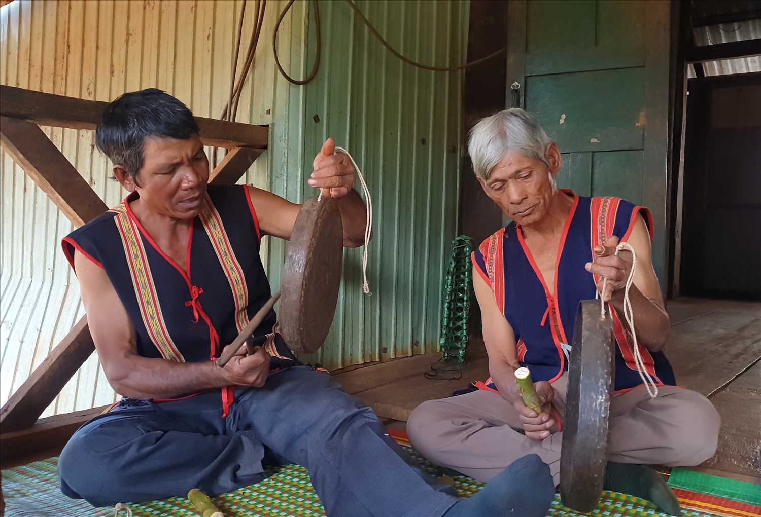 Già làng Rơ Châm Guk (bên trái) đang chỉ dạy lại nghề chỉnh chiêng cho những già làng khác