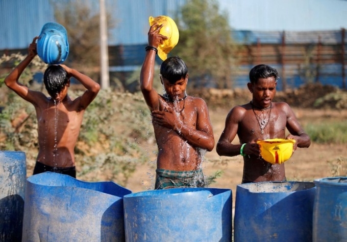 Công nhân dùng mũ bảo hộ múc nước tắm để giải nhiệt giữa cái nóng gay gắt ở ngoại ô thành phố Ahmedabad, Ấn Độ, ngày 30/4. Ảnh: Reuters.