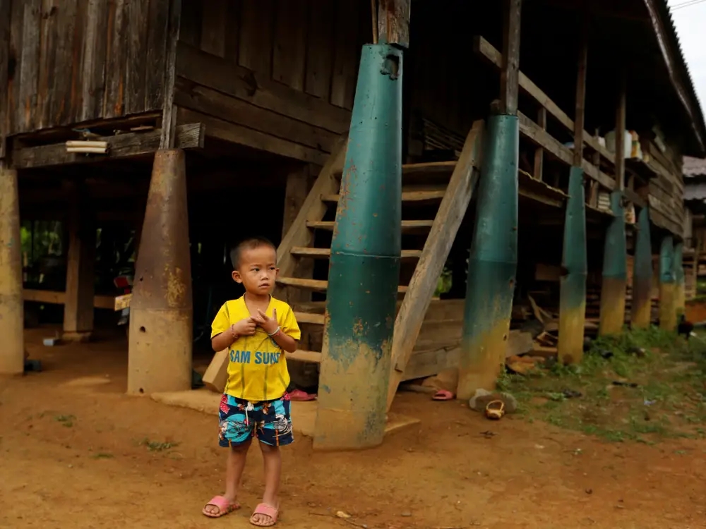 Cậu bé đứng trước ngôi nhà được xây bằng bom ở Xiêng Khoảng, Lào