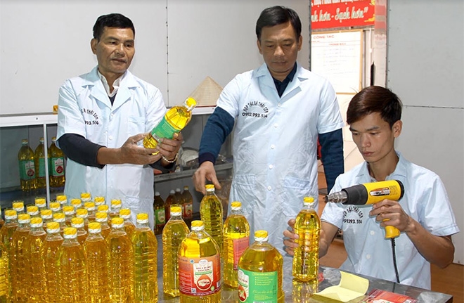 Ông Đàm Văn Việt, Chủ tịch Hội đồng Quản trị HTX Thái Sơn (đứng giữa) kiểm tra công đoạn đóng gói, dán tem sản phẩm dầu lạc đỏ (Ảnh: Báo Yên Bái)