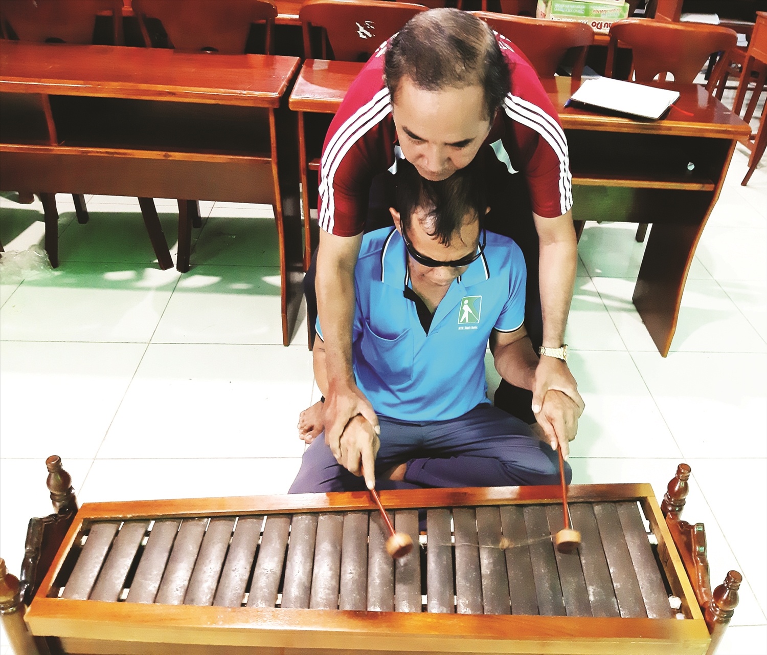 Nghệ nhân Lâm Minh Cường cầm tay chỉ dạy từng nốt nhạc cho học viên khiếm thị tham gia lớp học nhạc ngũ âm.