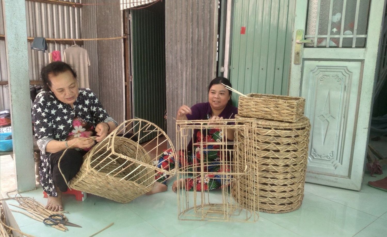 Chị Trần Kim Thùy (bìa phải) ở ấp Mỹ Tân, xã Mỹ Bình (thị xã Ngã Năm) nhận nguyên liệu lục bình đan giỏ về nhà những lúc rãnh rỗi, giúp chị có thêm thu nhập