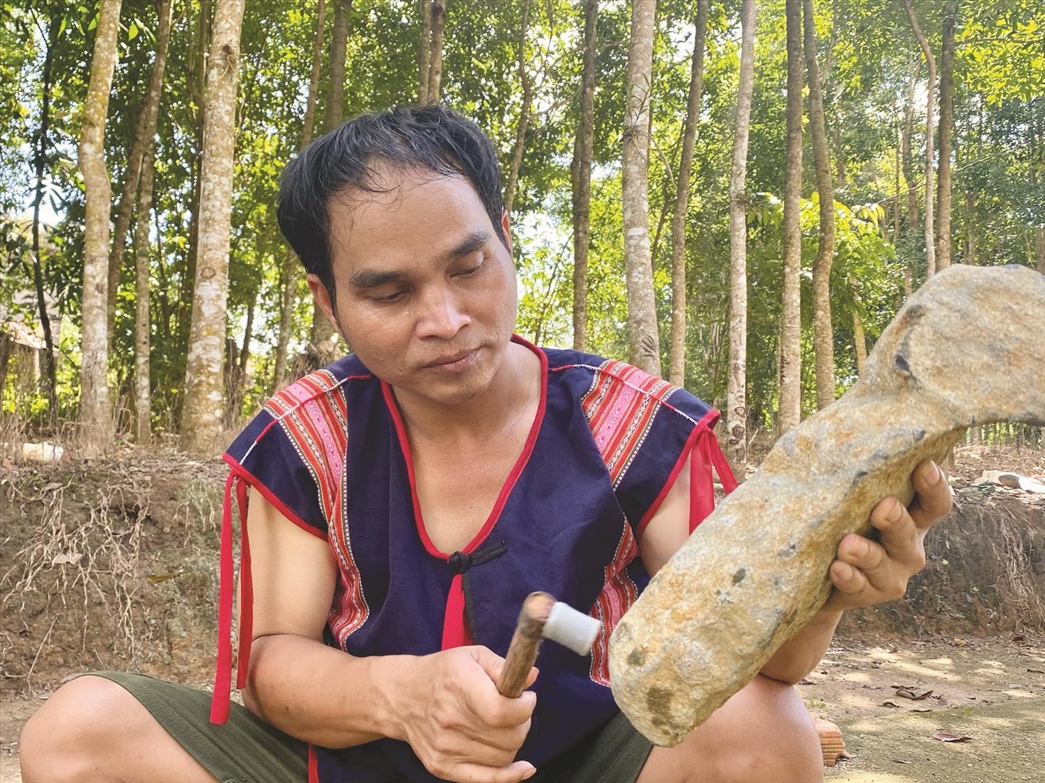 Nghệ nhân Ưu tú A Huynh cẩn thận gọt các thanh đá để chỉnh âm cho giàn đàn đá.