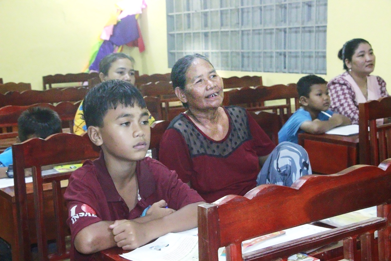 Bà Thị Long, 65 tuổi, đang ngồi học cùng đứa cháu ngoại tên Điểu Trường, 12 tuổi.