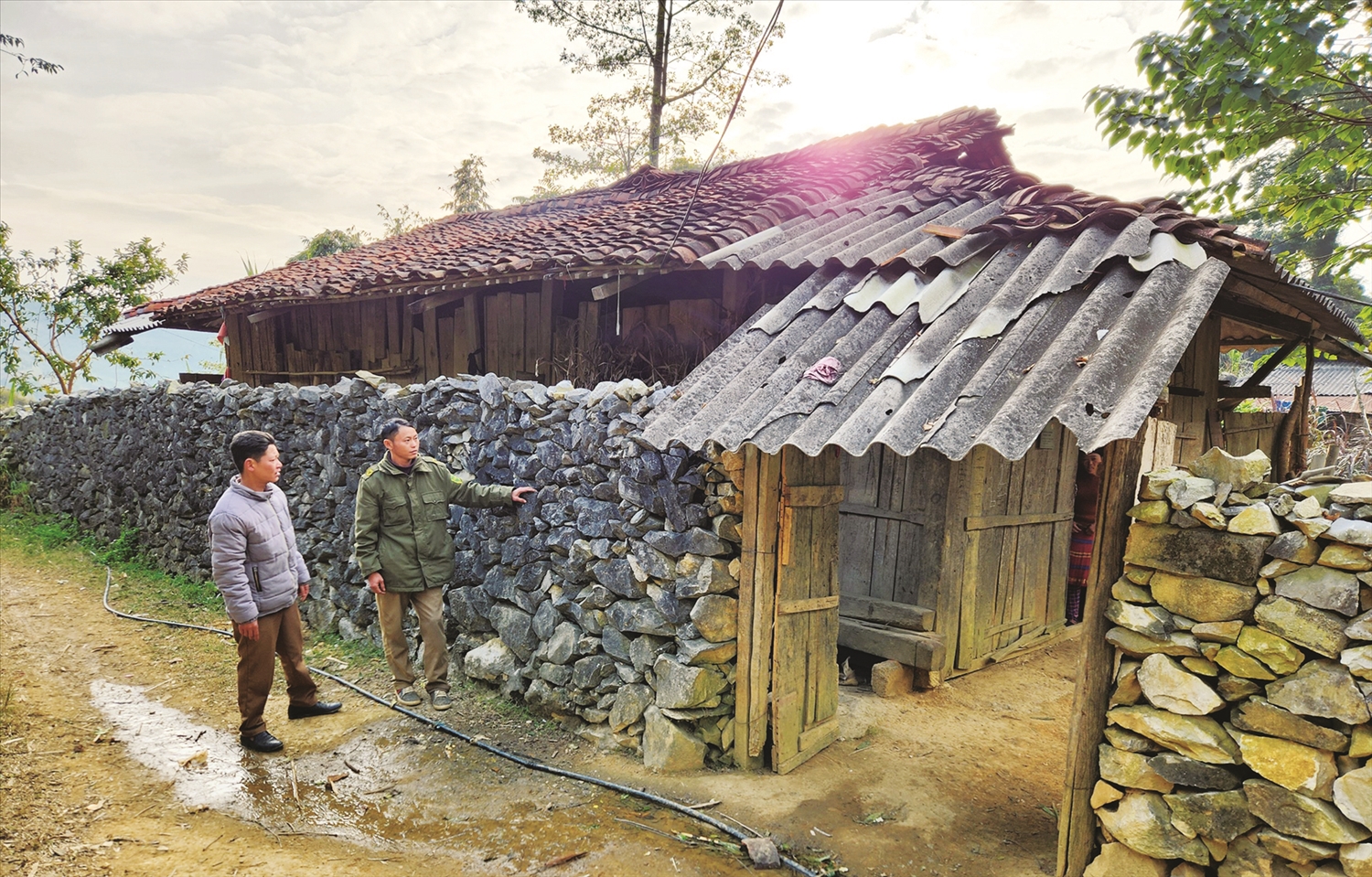Anh Vừ Mí Chá, dân tộc Mông ở xã Khâu Vai (mặc áo xanh) giới thiệu về tường rào đá và ngôi nhà lợp ngói âm dương của gia đình được làm hơn 20 năm. Ảnh: Quỳnh Lưu