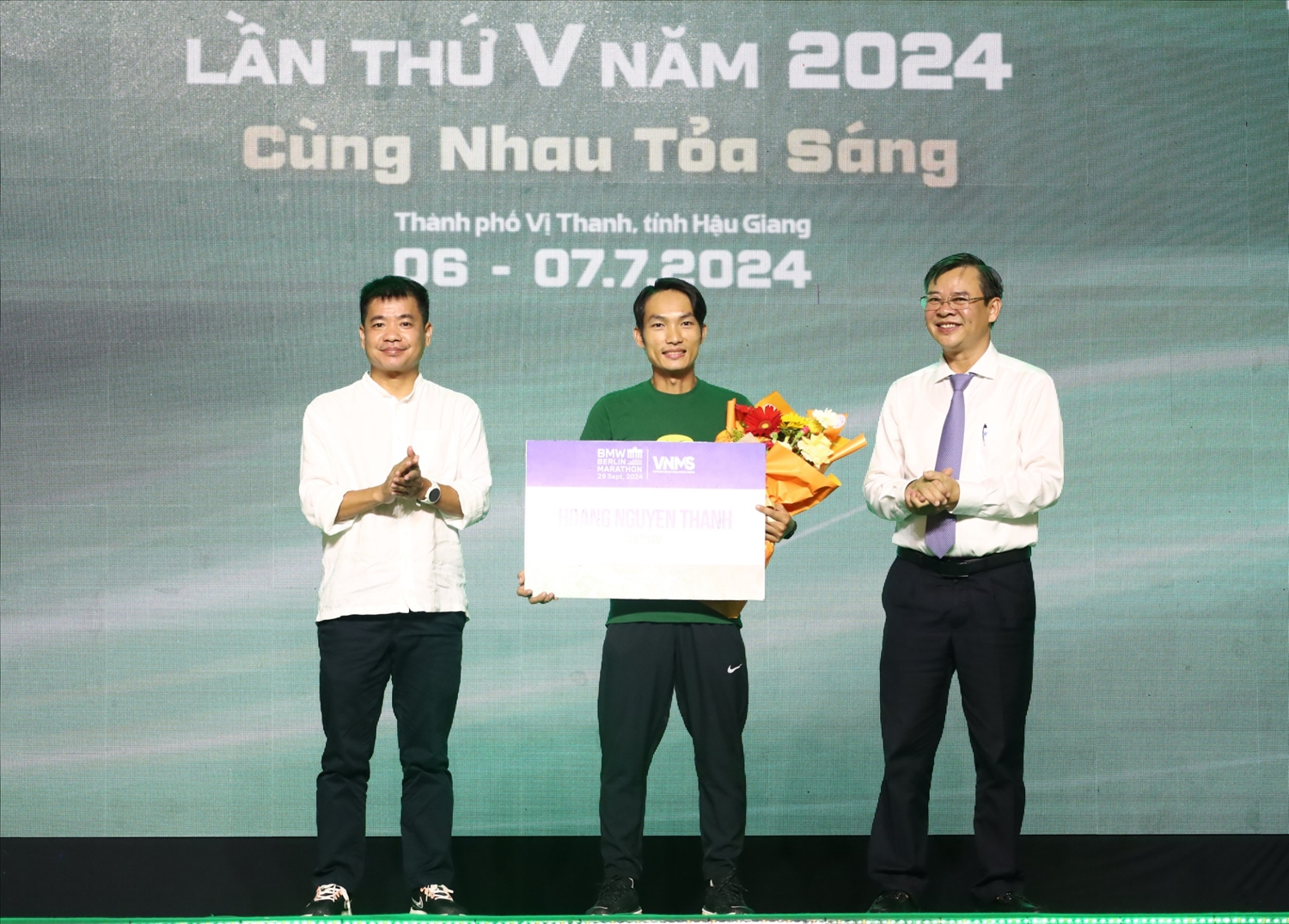 Phó Chủ tịch thường trực UBND tỉnh Hậu Giang Trương Cảnh Tuyên ( bìa phải) và ông Nguyễn Tử Anh, Giám đốc điều hành Công ty Cổ phần Truyền thông Nexus trao hoa và biểu trưng cho vận động viên Hoàng Nguyên Thanh tham gia du đấu giải Berlin Marathon