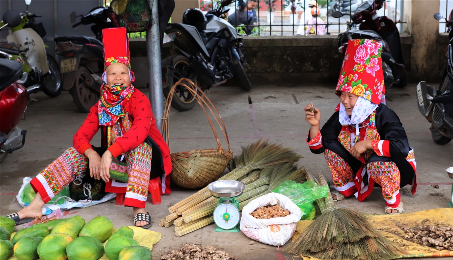 Người phụ nữ Dao Thanh Phán đã có chồng thường cạo trọc đầu, đội một hộp dài màu đỏ và phủ khăn hoạ tiết lên trên. Trong ảnh: Phụ nữ Dao Thanh Phán rực rỡ trong trang phục truyền thống, bày bán hoa quả, vật dụng do chính mình làm ra tại chợ phiên.