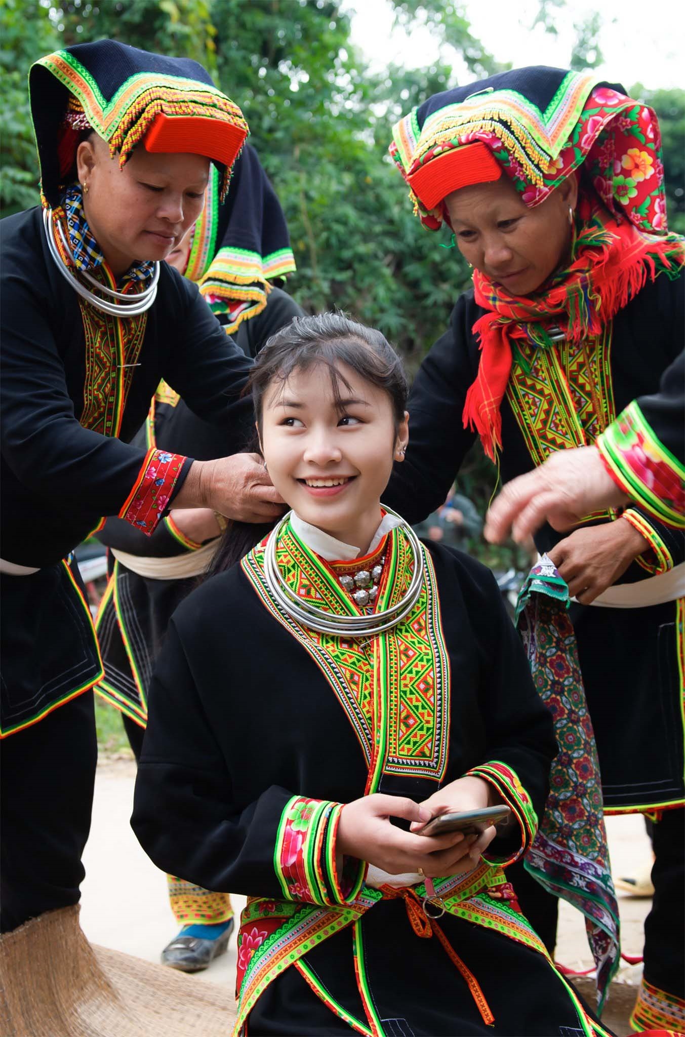 Trang phục cô dâu gồm khăn che mặt, áo nhiều lớp và bốn thắt lưng thêu hoa. Ngoài ra, cô dâu còn đội mũ, đeo vòng cổ, vòng tay và các đồ trang sức bằng bạc. (Trong ảnh là mế (mẹ) đoàn nhà gái chỉnh sửa trang phục cưới cho cô dâu Triệu Thị Tiên khi cách nhà chú rể Hoàng Hữu Thanh khoảng 100 m)