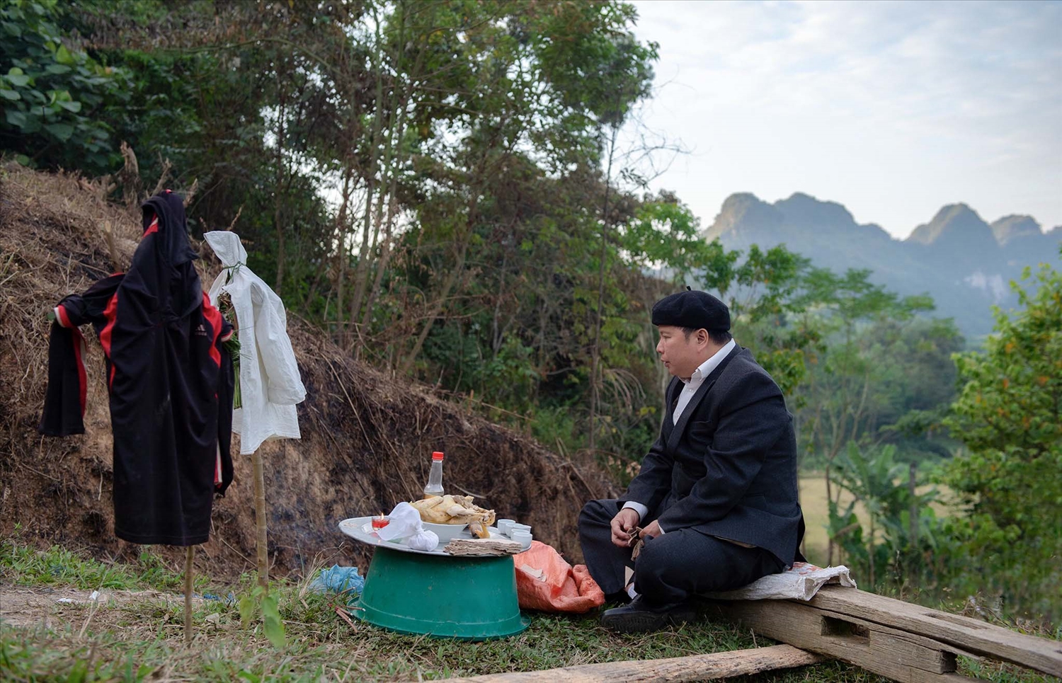 Thầy cúng đang làm lễ ngoài trời chuẩn bị đón đoàn nhà gái. Ngoài mâm cỗ cúng, còn có bộ quần áo hình nhân nam nữ.