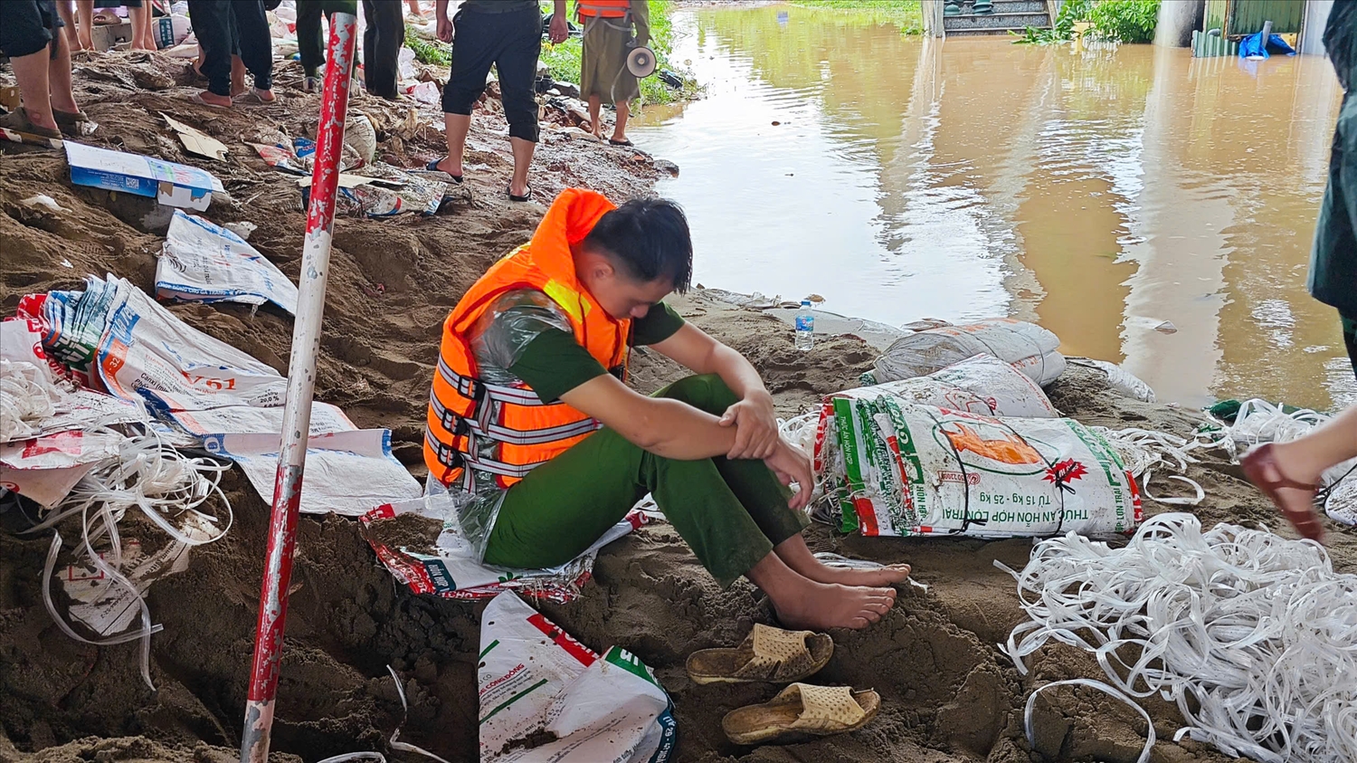 Sau nhiều giờ dầm mình trong nước, lực lượng hộ đê tranh thủ nghỉ ngơi ngay bên bờ đê để lấy sức tiếp tục nâng cao bờ đê thêm khoảng 50cm trước 14 giờ chiều nay. (Ảnh: Nguyễn Liên)