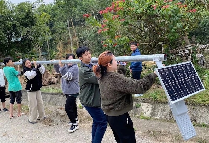 Các thành viên cùng người dân vận chuyển cột đèn đến những con ngõ nhỏ trong làng để lắp đặt. Ảnh: CTV