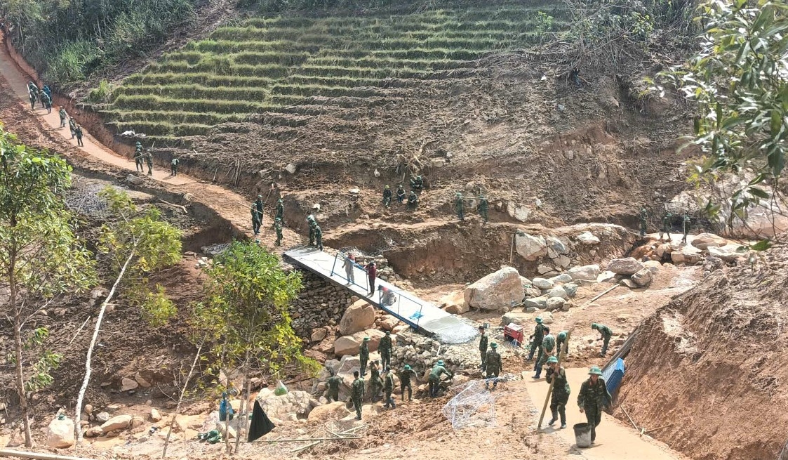 Lực lượng bộ đội và đồng bào Xơ Đăng chung tay làm cầu tạm bắt qua điểm sạt lở núi gây đứt đường lên 5 thôn của xã Ngọc Linh. (Ảnh: Ngọc Chí)
