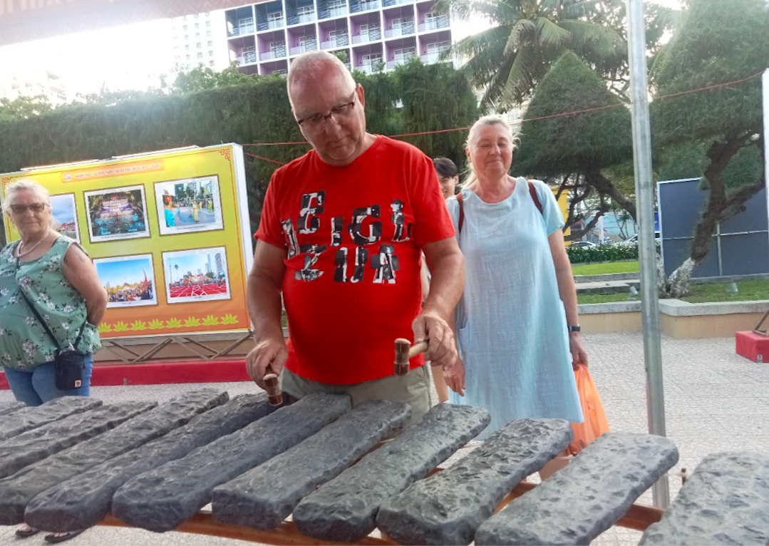 Du khách quốc tế trực tiếp trải nghiệm cách đánh đàn đá tại làng nghề Trường Sơn. (ảnh: X.H)