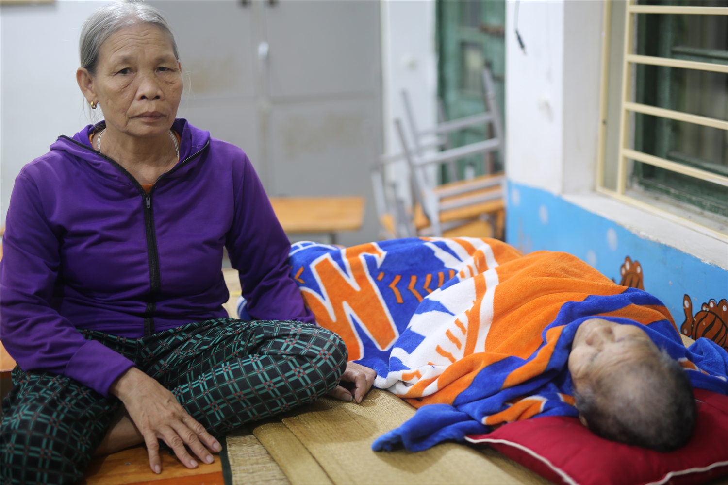 Bà Đậu Thị Minh (60 tuổi) ở xóm Quyết Thành đang chăm mẹ chồng Phạm Thị Năm nằm liệt một chỗ tại nơi tránh trú bão của xã Diễn Châu - Ảnh: Thanh Hải