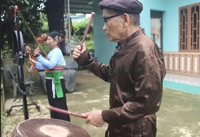 Nghệ nhân Ưu tú Phạm Vũ Vượng chỉ dạy cho bà Phạm Thị Hòa đánh cồng chiêng (Ảnh Kiều Huyền)