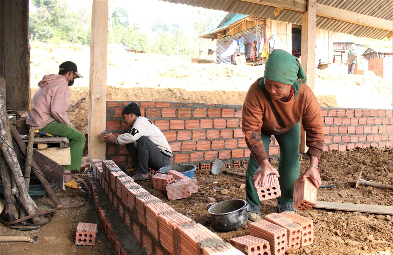 Bà Y Mâm (ngoài cùng bên phải) tham gia chuyển gạch để con cháu giúp xây dựng lại nhà mới. (Ảnh: Ngọc Chí) 