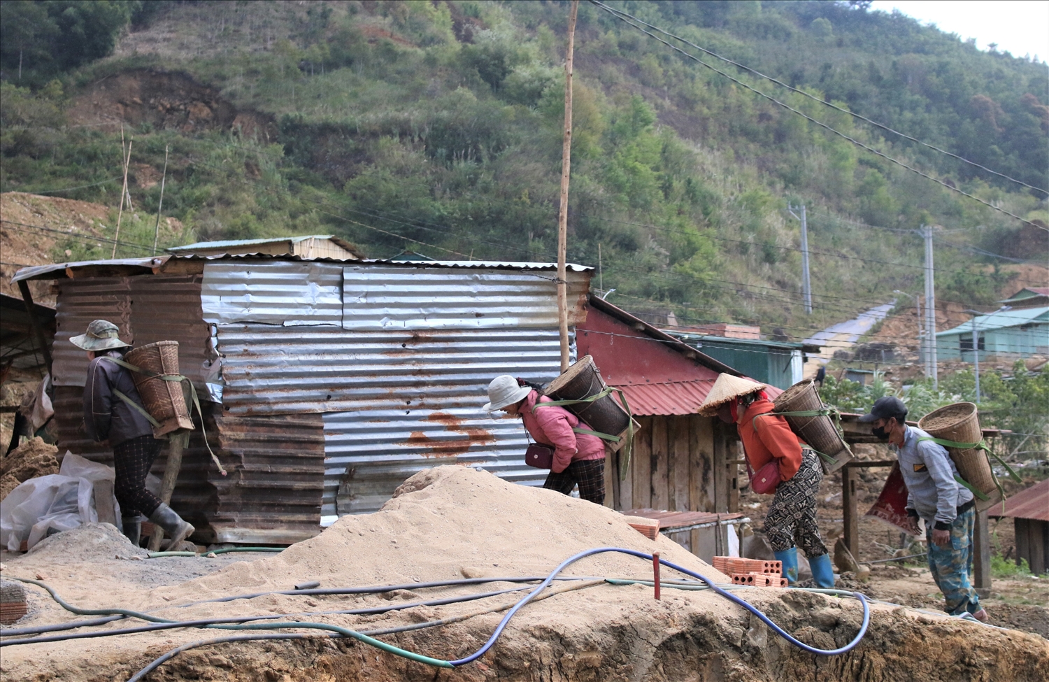 Do địa hình đồi dốc, đồng bào Xơ Đăng làng Chum Tam phải gùi vật liệu lên khu tái định cư để xây dựng nhà. (Ảnh: Ngọc Chí)