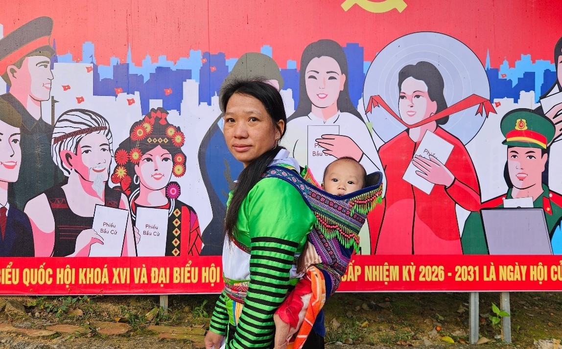 Cử tri xã Nhi Sơn địu con đến khu vực bỏ phiếu, thực hiện quyền và nghĩa vụ công dân.(ảnh Quỳnh Trâm).