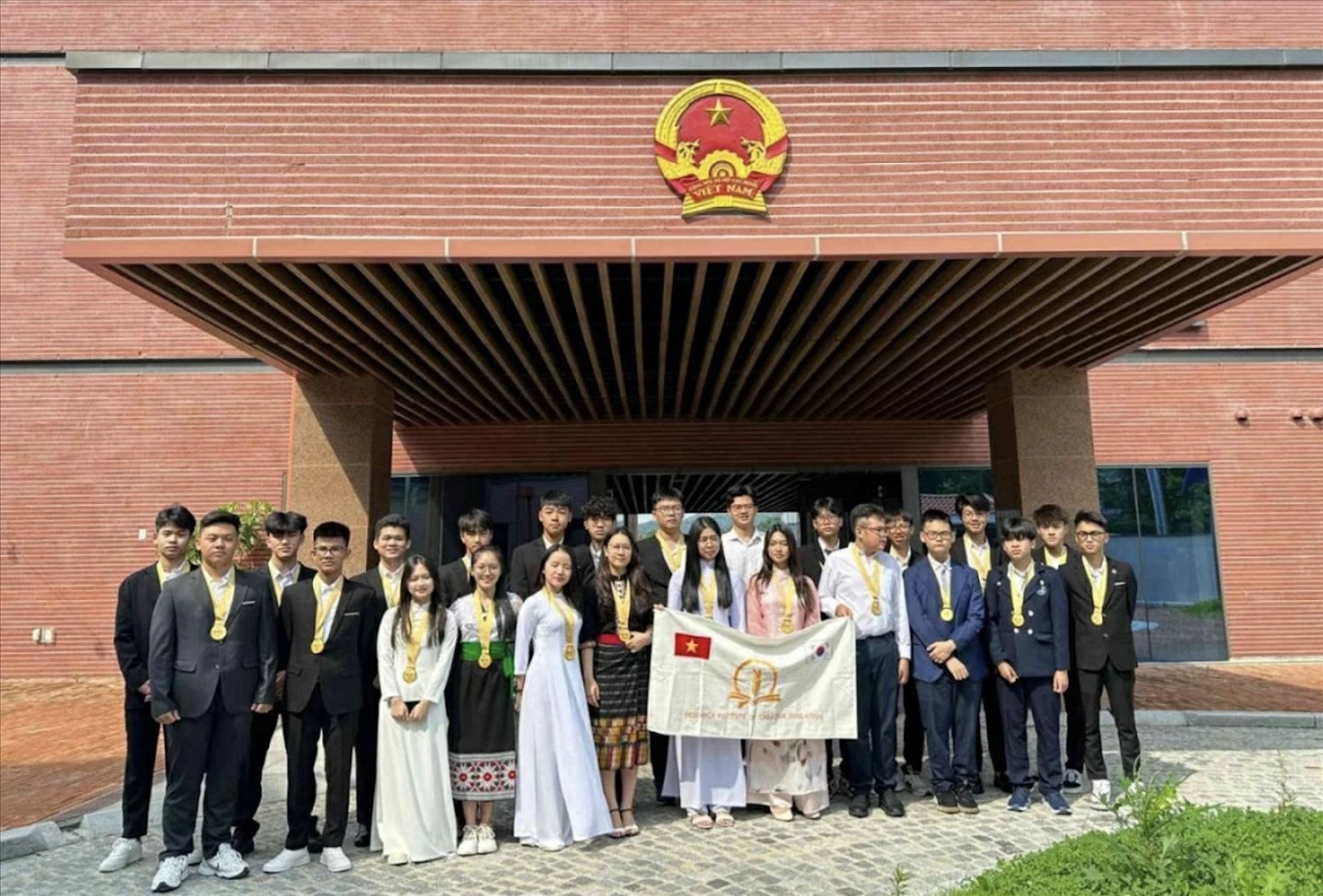 Hà Anh (váy Thái đen, đứng bên trái lá cờ) chụp ảnh cùng đoàn Việt Nam tại Đại sứ quán Việt Nam tại Hàn Quốc trong khuôn khổ tham dự Olympic Phát minh và sáng tạo thế giới WICO 2023 (WICO) tổ chức tại Hàn Quốc.