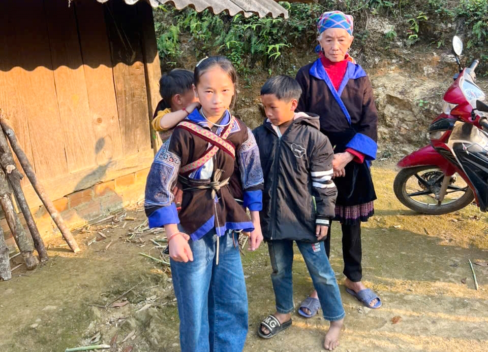 Cụ Mùa Thị Dở gầy guộc cùng ba cháu nhỏ đứng trước ngôi nhà gỗ tuềnh toàng, nơi bão tố cuộc đời vừa ập xuống