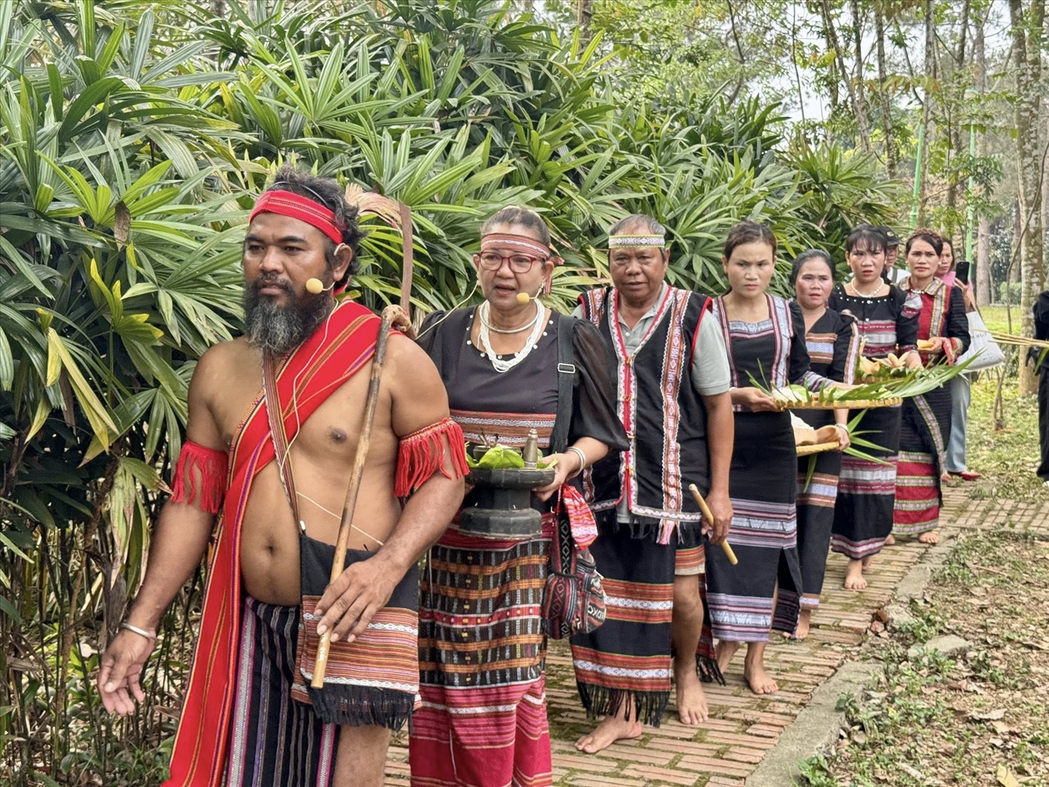 Già làng dẫn đầu đoàn rước lễ từ nhà già làng và người dân mang lễ vật tiến về nhà dài cộng đồng.