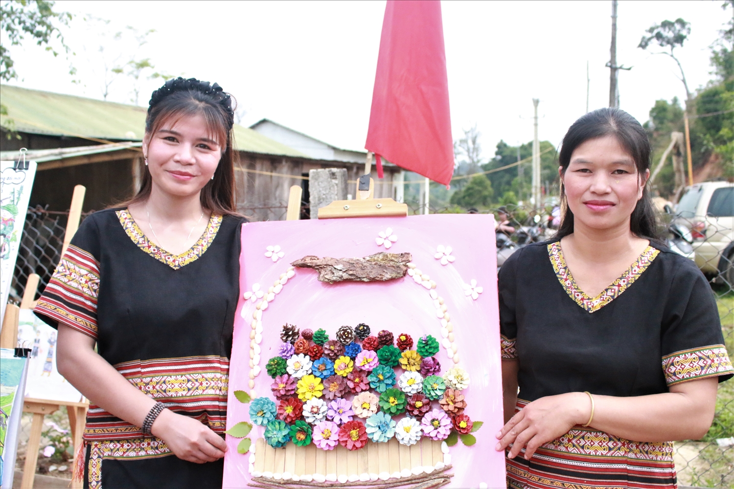 Phụ nữ Làng du lịch cộng đồng Kon Plông giới thiệu những bức tranh được làm từ trái thông đang trưng bày tại nhà văn hóa làng. (Ảnh: Ngọc Chí)